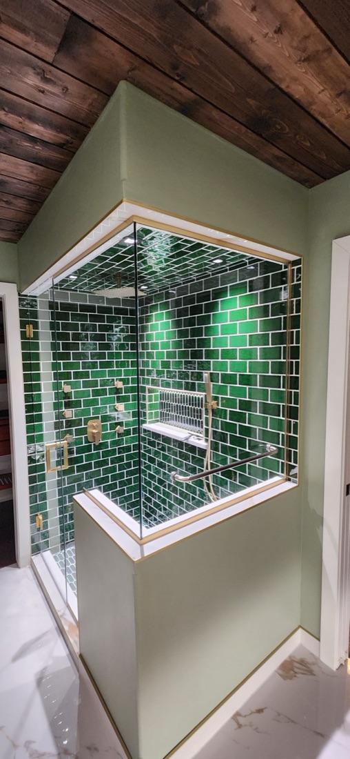 Emerald-green shower tile and warm metal fixtures framed by white marble-look tile in South River Jewel