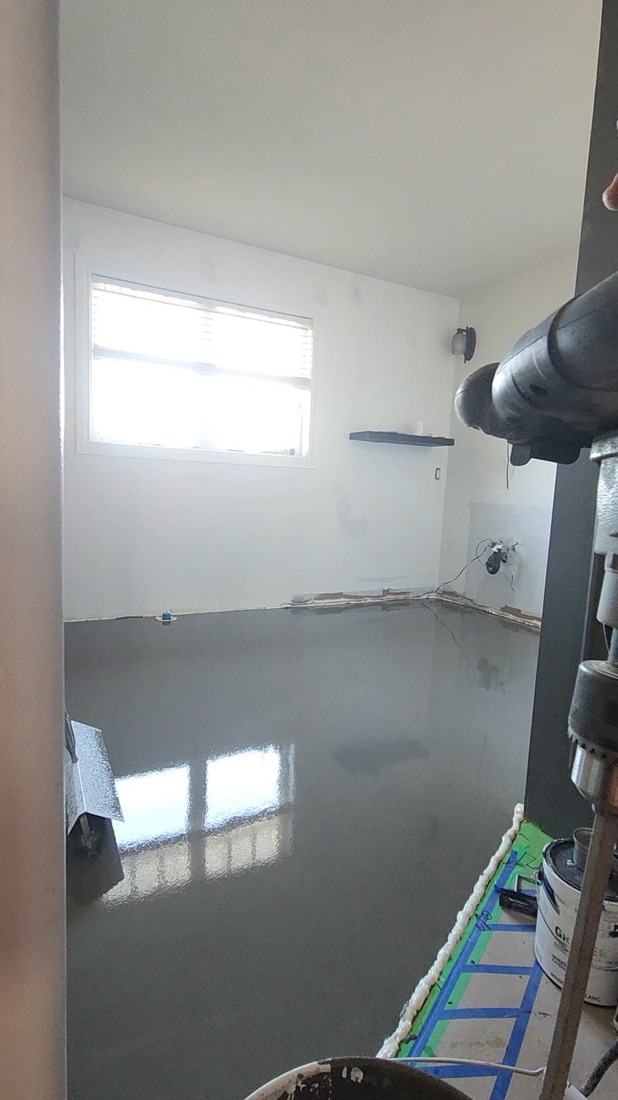 Fresh self-levelling underlayment across the Luminous Smoke floor reflecting the window after the pour