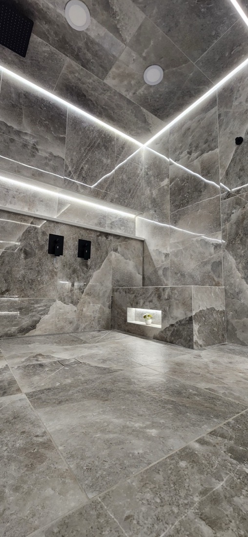 Matte Rock Salt Smoke shower-floor tile below large-format walls, a tiled bench and illuminated niche in Luminous Smoke